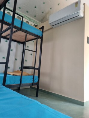 Una cama litera con ropa de cama azul, un aire acondicionado blanco y un techo estampado.