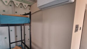 A bunk bed with a blue mattress and a brown blanket, a white air conditioner, and a patterned ceiling.