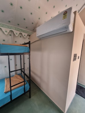 A bunk bed with a blue mattress and a brown blanket, a white air conditioner, and a patterned ceiling.