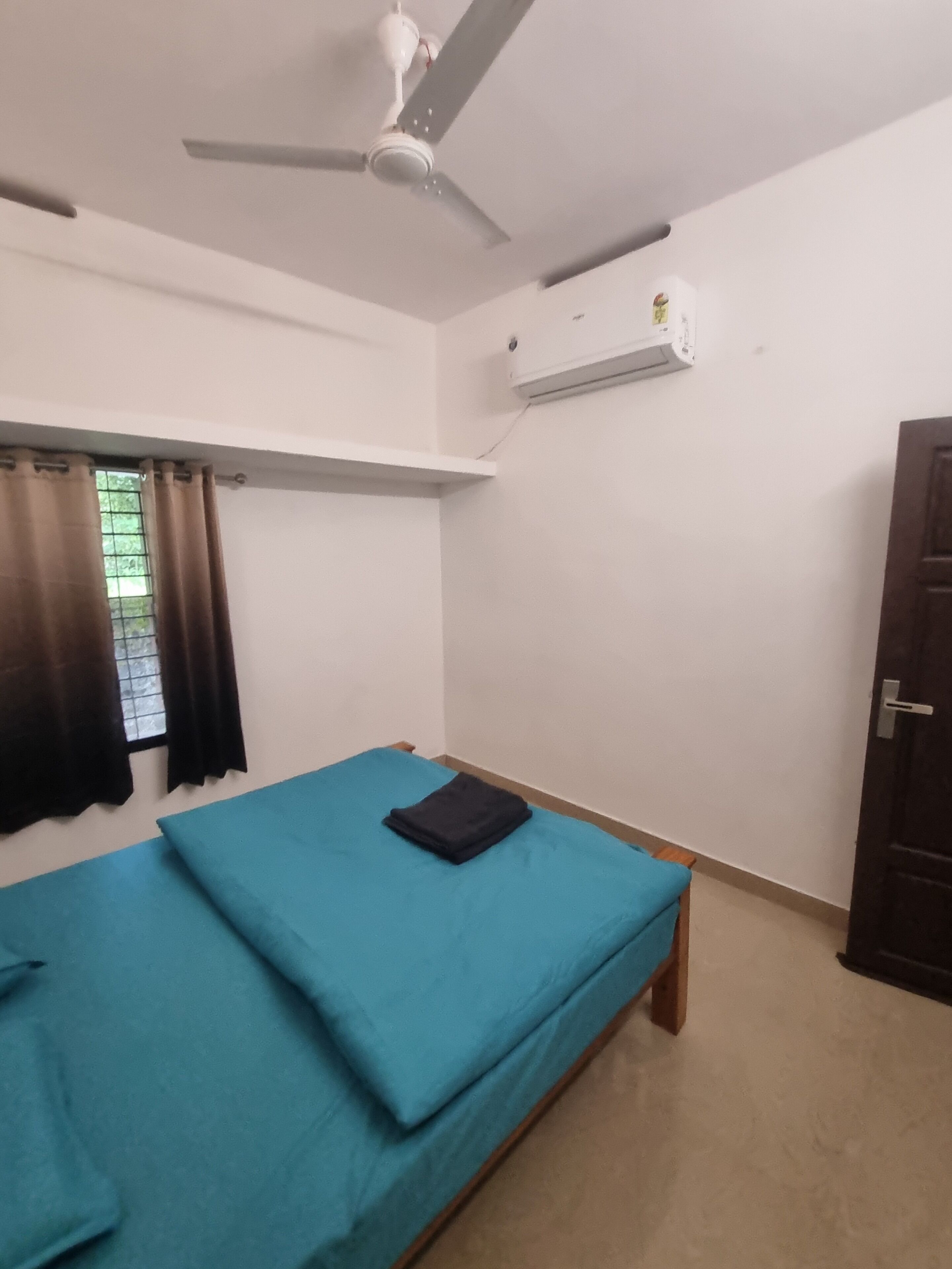 Una habitación con cama, ventilador de techo, aire acondicionado y una ventana con cortinas.