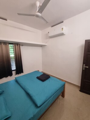 A room with a bed, a ceiling fan, an air conditioning unit, and a window with curtains.