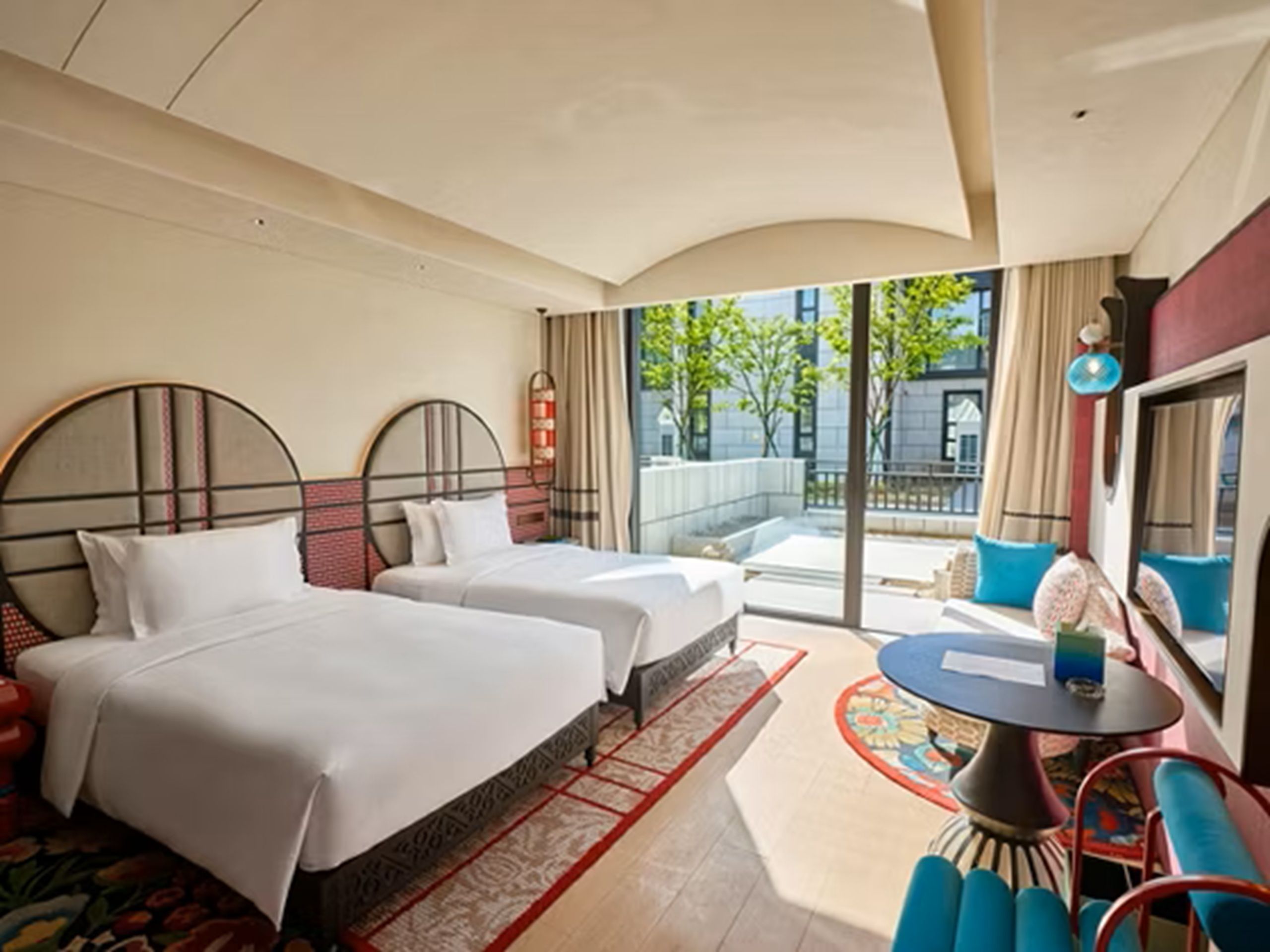 A hotel room with two beds, a small round table, and a view of the outside.
