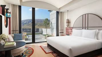 A modern hotel room with a large bed, a round table, and a view of the mountains.
