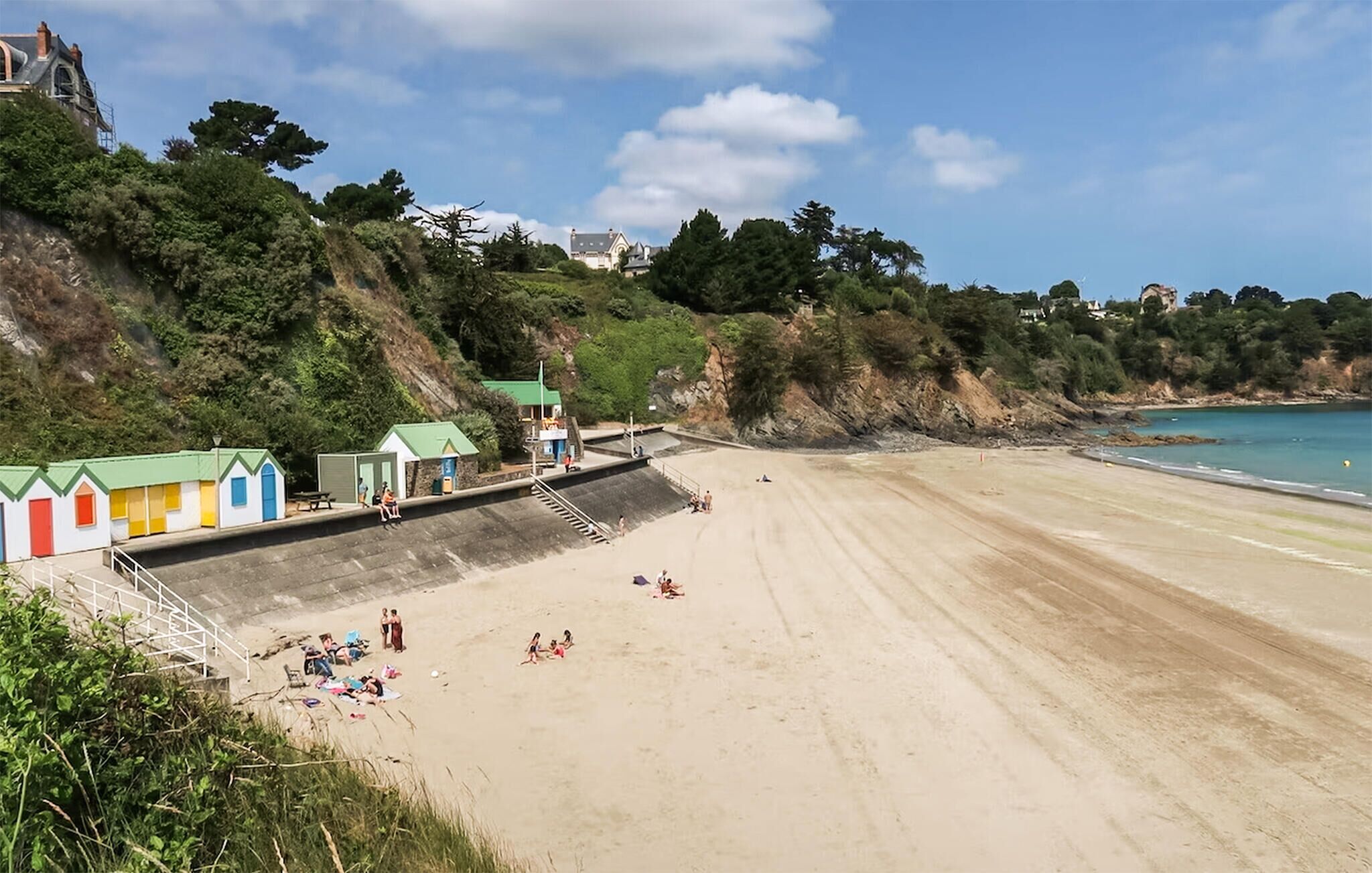 A beach with a concrete walkway leading to a row of colorful beach huts.