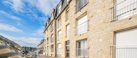 Una hilera de edificios de piedra con balcones, una calle adoquinada y un coche estacionado.