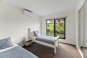 Ein Schlafzimmer mit zwei Betten, einem Nachttisch und einem Fenster mit Blick auf einen Garten.