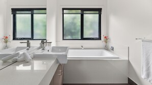Un baño moderno con dos lavamanos, una bañera y ventanas con vidrio esmerilado.