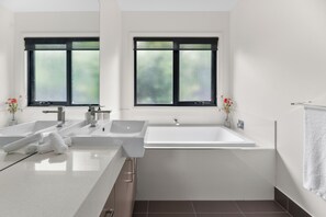 Ein modernes Badezimmer mit zwei Waschbecken, einer Badewanne und Milchglasfenstern.