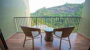 Een balkon met rieten stoelen en een glazen tafel, met uitzicht op een bergachtig landschap.