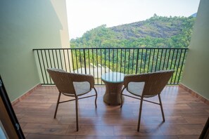 A balcony with wicker chairs and a glass table, overlooking a mountainous landscape. - Studio resort in peaceful Wayanad with AC comfort (wayanad)