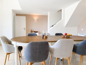 Un comedor moderno con una mesa de madera redonda, seis sillas tapizadas y una lámpara sobre la mesa.