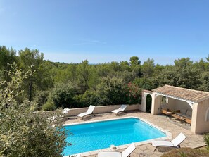 Una piscina con sillas de descanso, un espacio de estar techado y vistas a un paisaje boscoso.