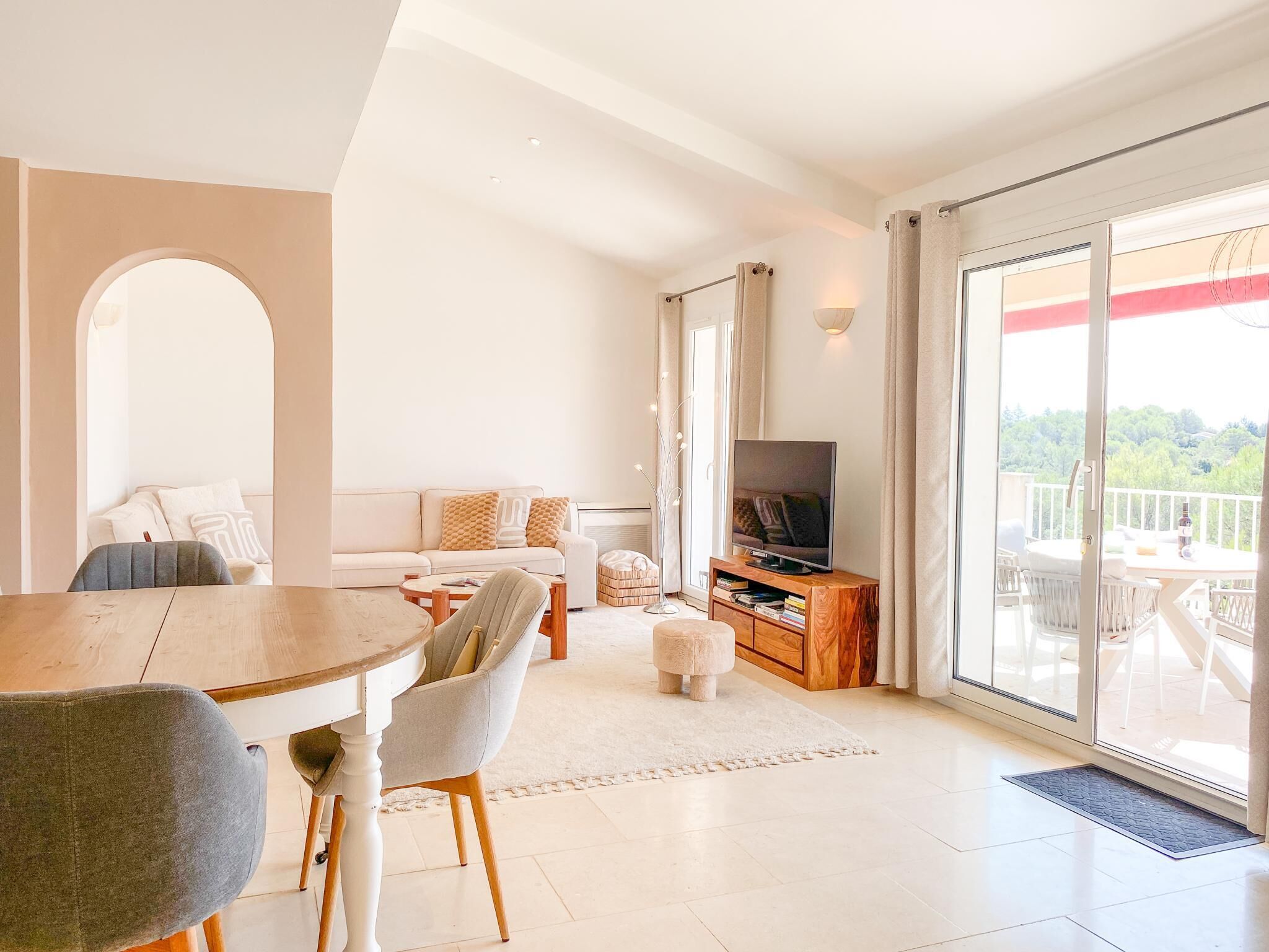 A modern living room with a dining table, sofa, TV, and a balcony with a view.