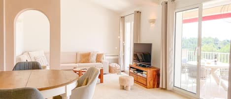 A modern living room with a dining table, sofa, TV, and a balcony with a view.