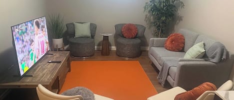 A living room with a television, two grey armchairs, a sofa, a coffee table, and a rug.
