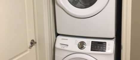 Máquina de lavar e secar empilhadas no canto de um cômodo com uma porta branca.