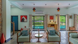 Amplia sala de estar con un ventanal a una piscina, dos sillones tapizados, una mesa de centro y un jarrón rojo.
