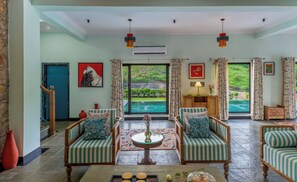 A spacious living area with a large window overlooking a pool, two upholstered armchairs, a coffee table, and a red vase.