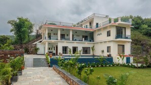 Una villa de dos pisos con piscina, mobiliario exterior y una escalera de piedra.