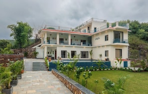 A two-story villa with a swimming pool, outdoor seating, and a stone staircase.
