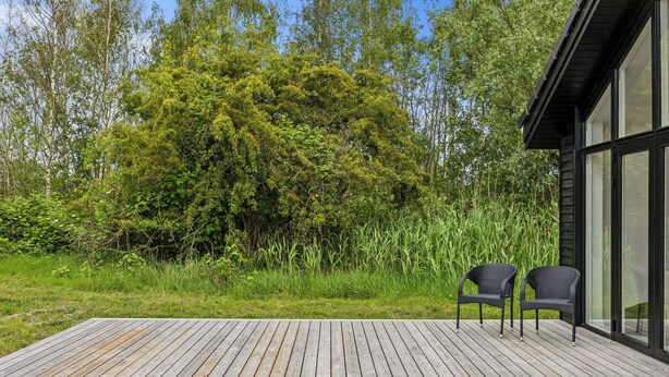 A wooden deck with two wicker chairs, surrounded by lush greenery and a large tree.