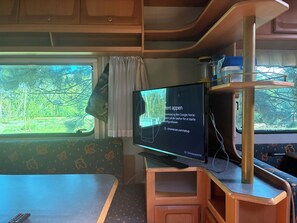 A television with a message on the screen, a wooden cabinet, a window with a view of trees, and a remote control on a table.