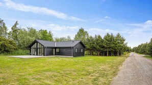 A modern two-story house with a sloped roof, large windows, and a gravel driveway. - New & inviting holiday home near beach and nature (Væggerløse)