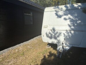 Un camper bianco parcheggiato accanto a una casa con una finestra e un'uscita.