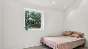 A small, single-bed room with a window, a plant, and a bed with a textured blanket.