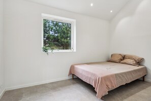 A small, single-bed room with a window, a plant, and a bed with a textured blanket.