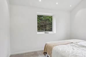 A bedroom with a single bed, a window with a view of trees, and a small plant on the windowsill.