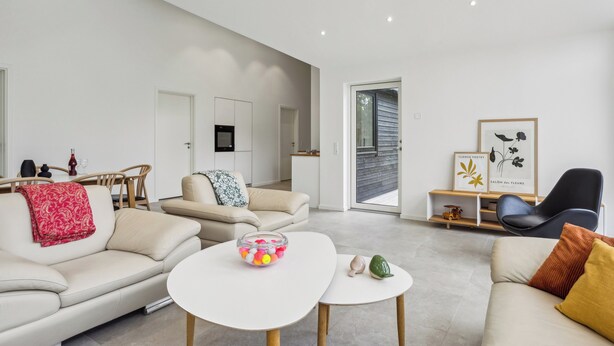 A modern living room with a sofa, a coffee table, and a dining area with chairs. - New & inviting holiday home near beach and nature (Væggerløse)
