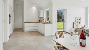 A modern kitchen with white cabinetry, a wooden countertop, and a dining area with a table and chairs. - New & inviting holiday home near beach and nature (Væggerløse)