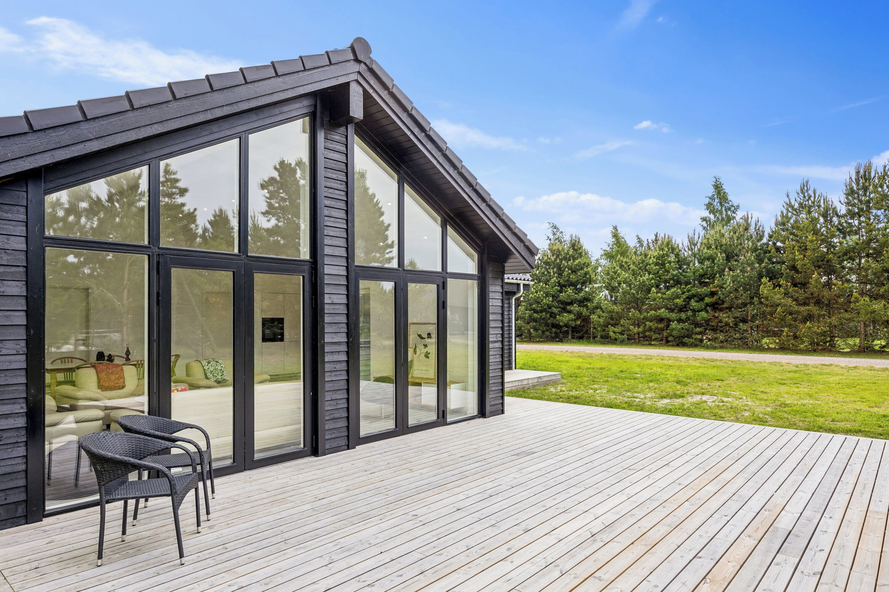 A modern house with large glass windows, a wooden deck, and outdoor furniture.