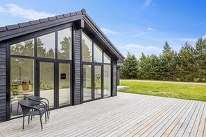 A modern house with large glass windows, a wooden deck, and outdoor furniture.