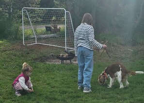 A person with a dog in a grassy area with a fenced enclosure in the background. - New & inviting holiday home near beach and nature (Væggerløse)