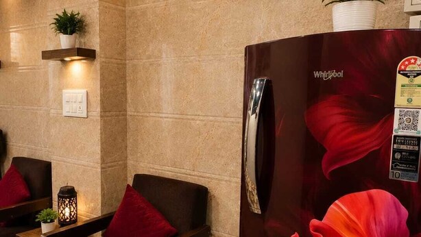 Un hall de hotel con pared de mármol, un reloj, un refrigerador con diseño floral y una zona de estar con mesa y sillas.