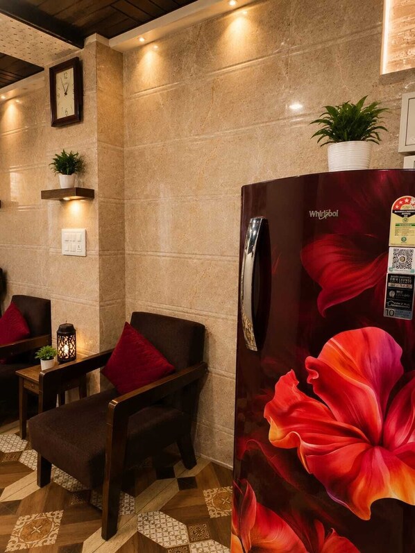 A hotel lobby with a marble wall, a clock, a refrigerator with a floral design, and a seating area with a table and chairs.