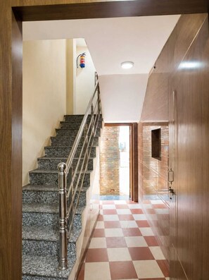 A staircase with a metal railing leading to a room with a checkered floor and a wooden door. - Krishna Inn Durgakund (Varanasi)