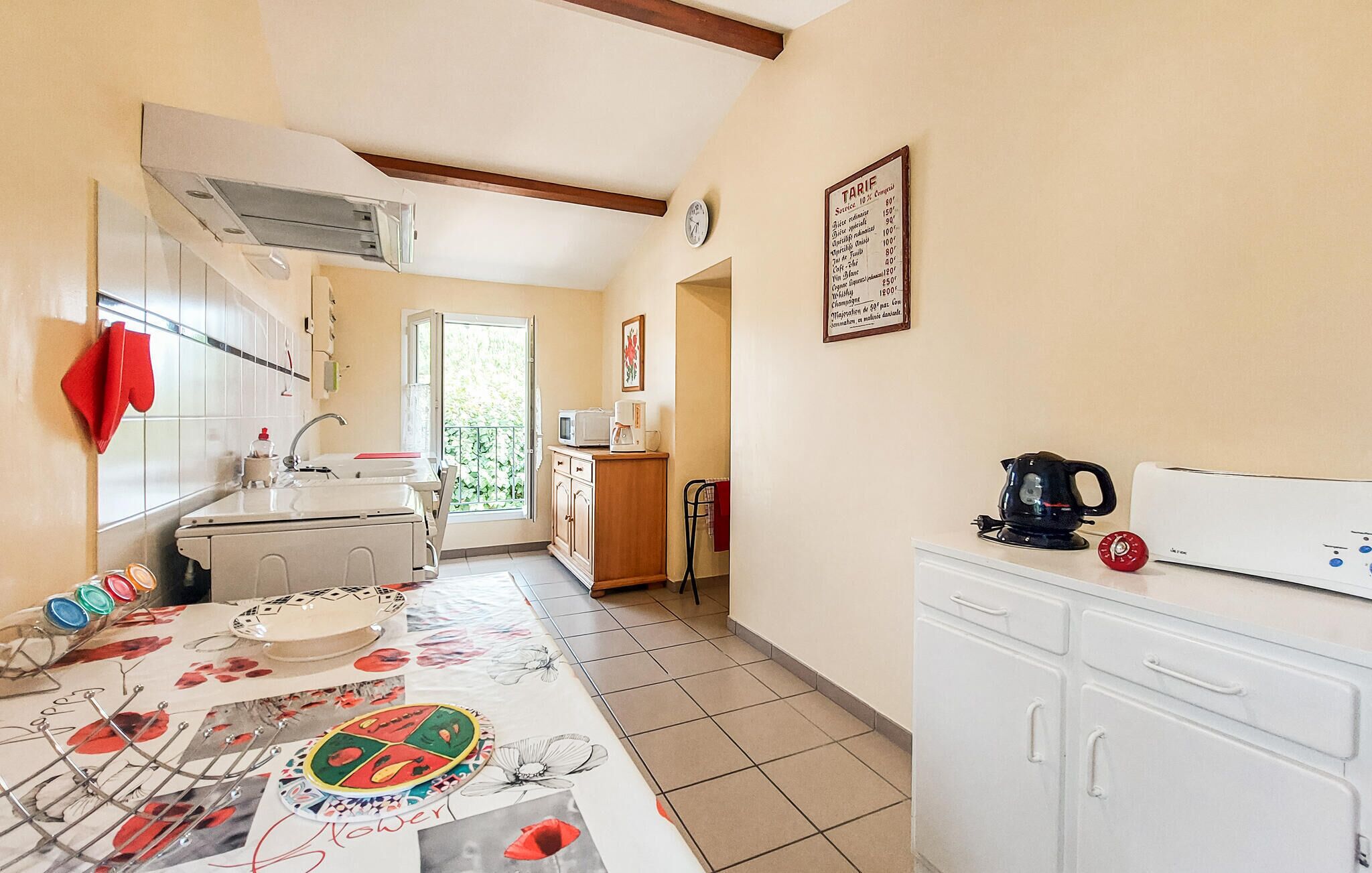 A kitchen with a dining table, cabinets, a clock, and a window.
