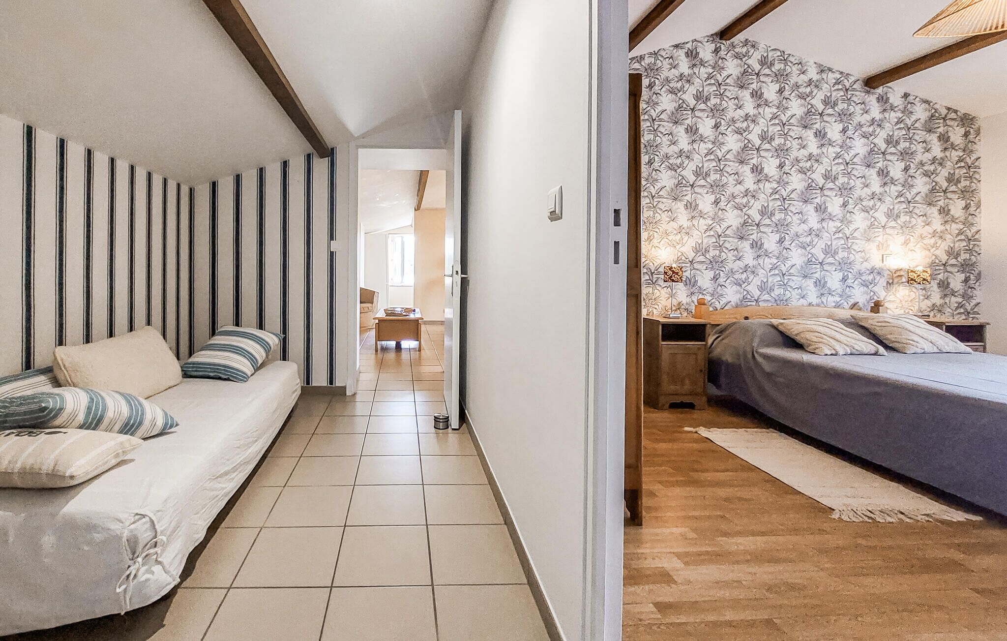 Een smalle gang die leidt naar een slaapkamer met een bed, een nachtkastje en een wand met bloemenbehang.
