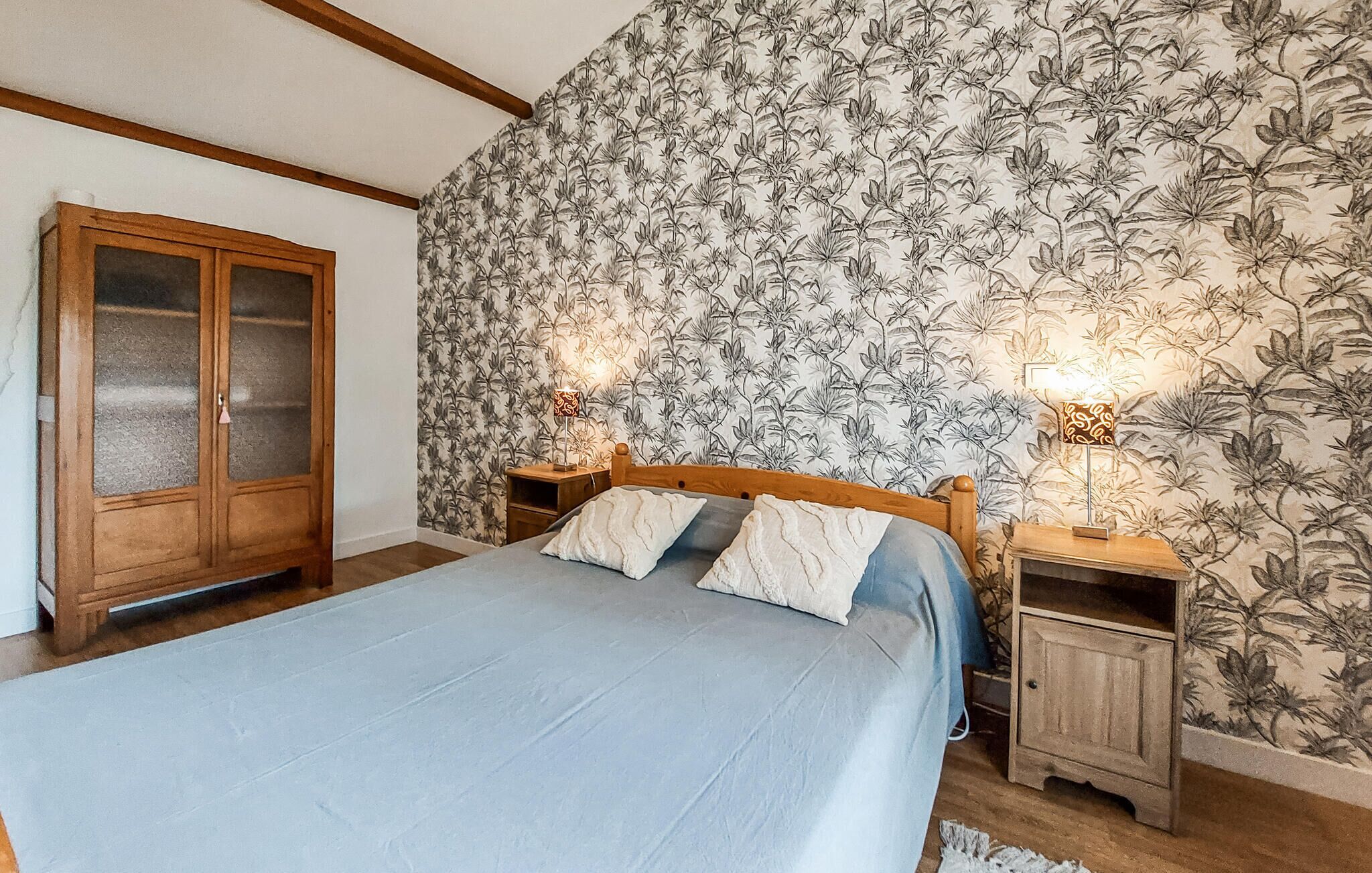 A bedroom with a bed, two bedside tables with lamps, a wardrobe, and floral wallpaper.