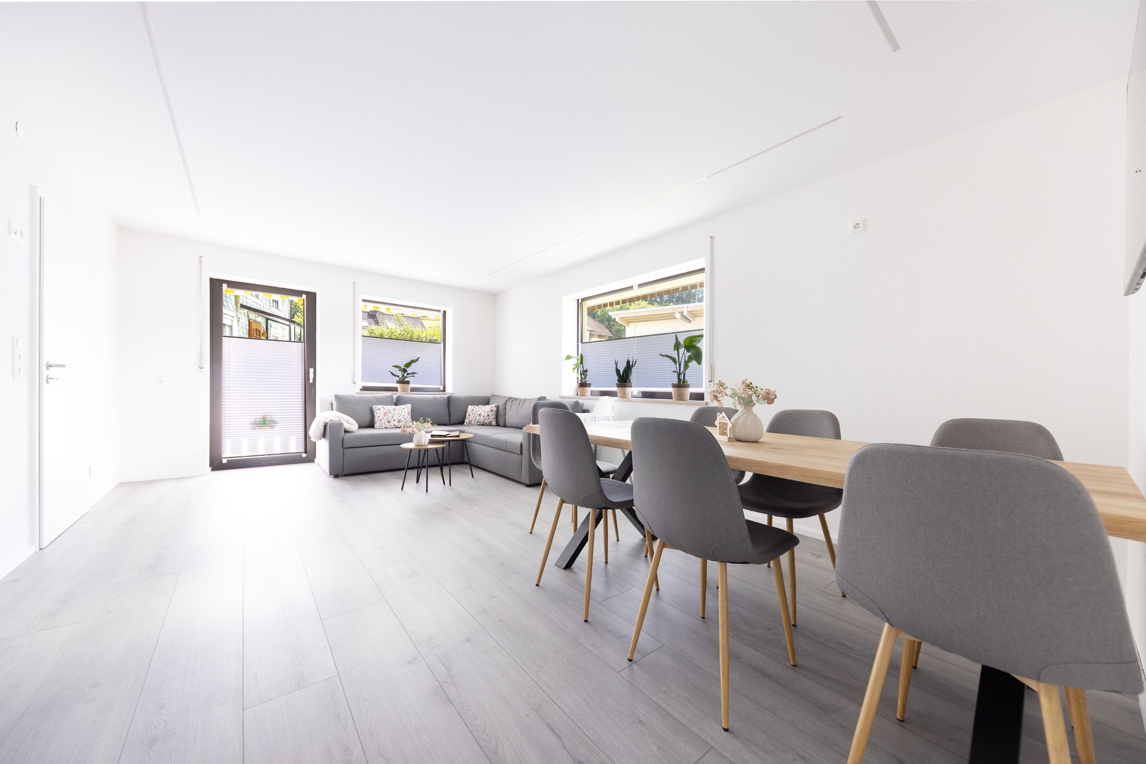 A modern living space with a dining area, grey sofas, and a wooden table with chairs.