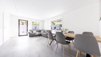 A modern living space with a dining area, grey sofas, and a wooden table with chairs.