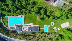 Een luchtbeeld van een resort met een groot zwembad, een tennisbaan en een speeltuin voor kinderen.