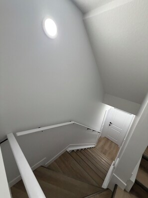 A staircase with a wooden finish, white walls, and a ceiling light. - The Quarry Retreat | Modern 2-Bedroom Luxury Suite (Edmonton)