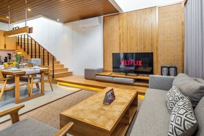 A modern living room with a wooden staircase, a dining area, and a flat-screen TV displaying 'NETFLIX'. - The Louver Canggu Exotic Bali Properties (Canggu)