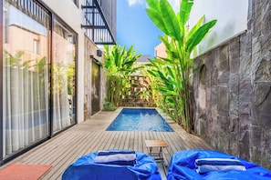 A pool area with a wooden deck, lounge chairs, and tropical plants. - The Louver Canggu Exotic Bali Properties (Canggu)