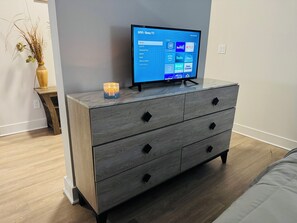 Een moderne kamer met een flatscreen televisie op een houten dressoir, een vaas met gedroogde planten en een brandende kaars.