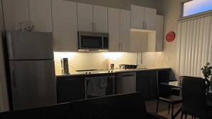 Una cocina moderna con armarios blancos, microondas, refrigerador y un comedor con mesa y sillas.